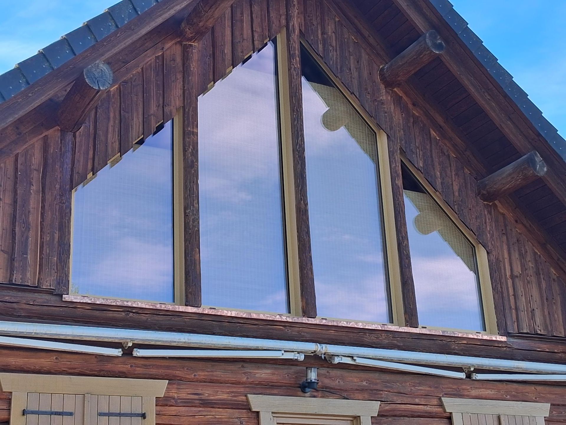 Pignon d’une cabane en bois avec de hautes fenêtres reflétant un ciel bleu