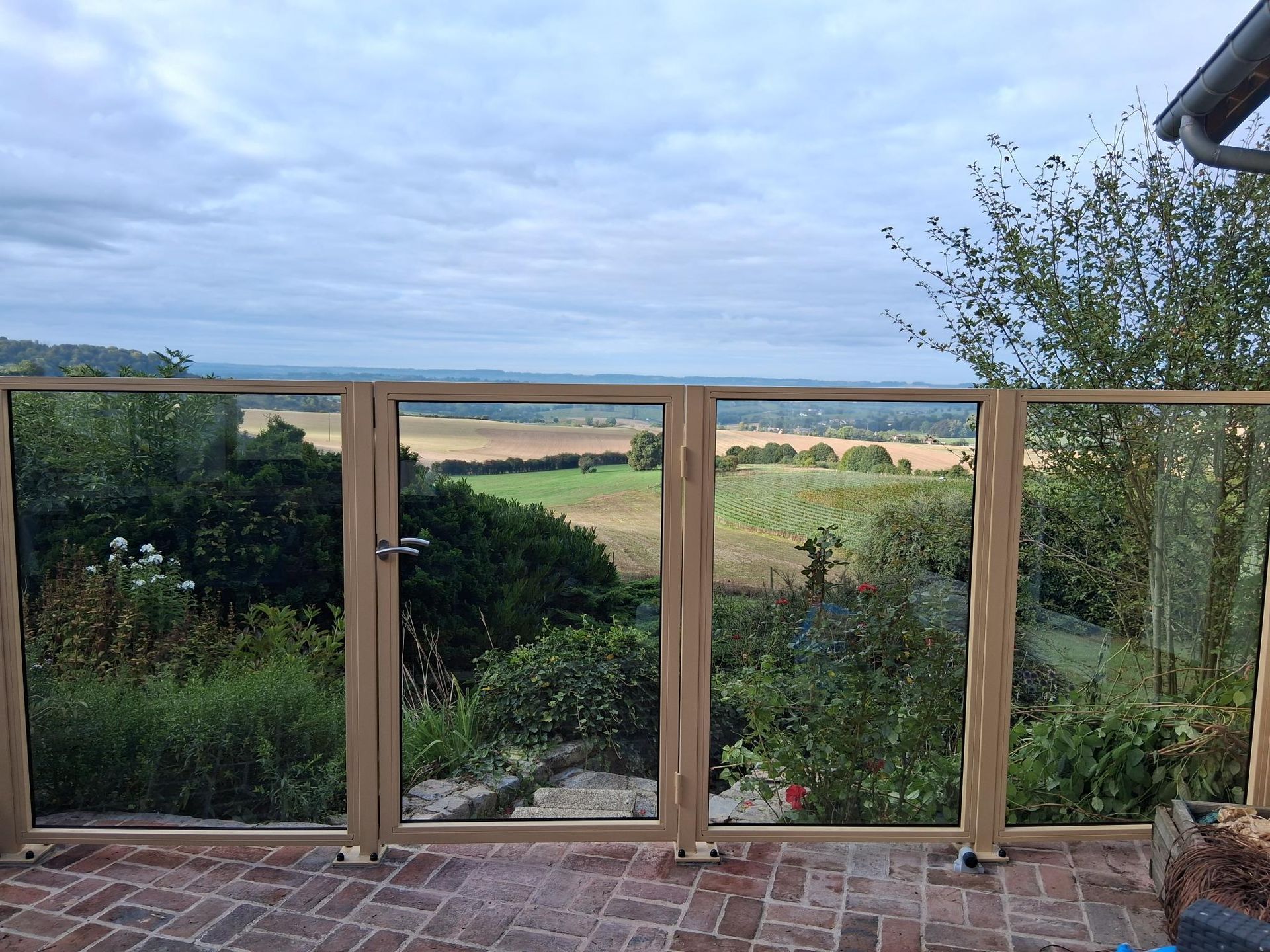 Garde-corps de balcon en verre donnant sur un champ verdoyant et un ciel nuageux
