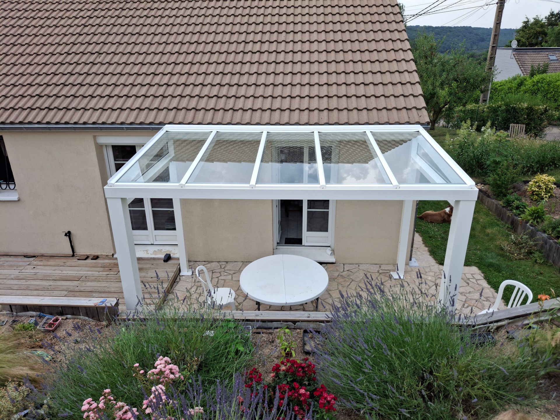 Patio arrière avec une pergola blanche, une table ronde et un jardin à côté d’une maison