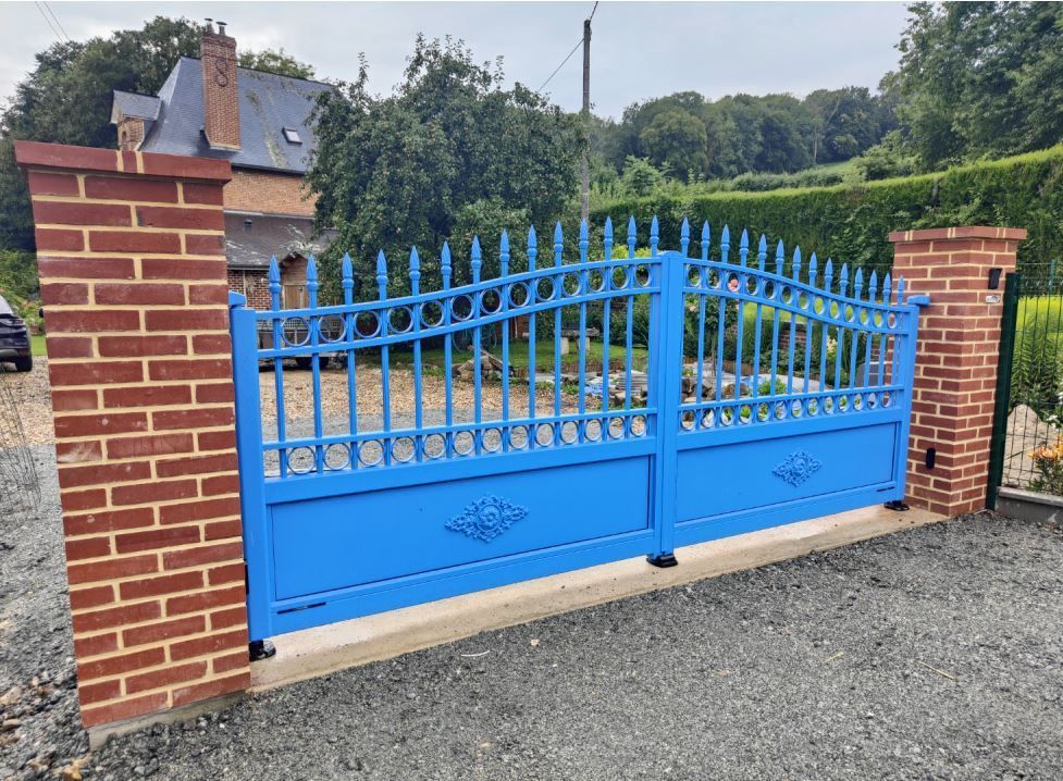 Portail d’entrée bleu en métal entre des piliers en brique, devant une maison et un jardin