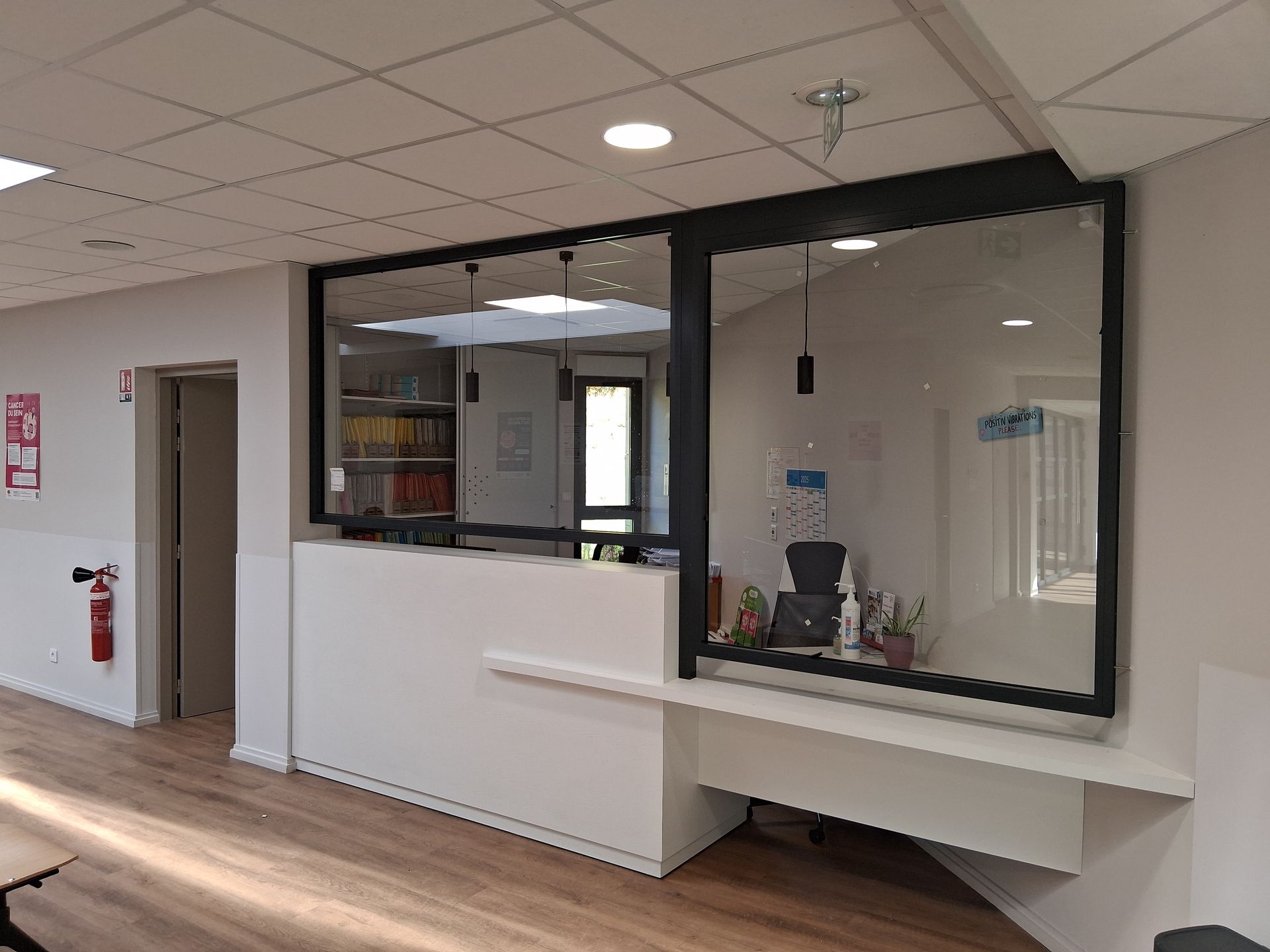 Couloir d’hôpital avec un comptoir d’accueil blanc et une fenêtre vitrée à cadre noir