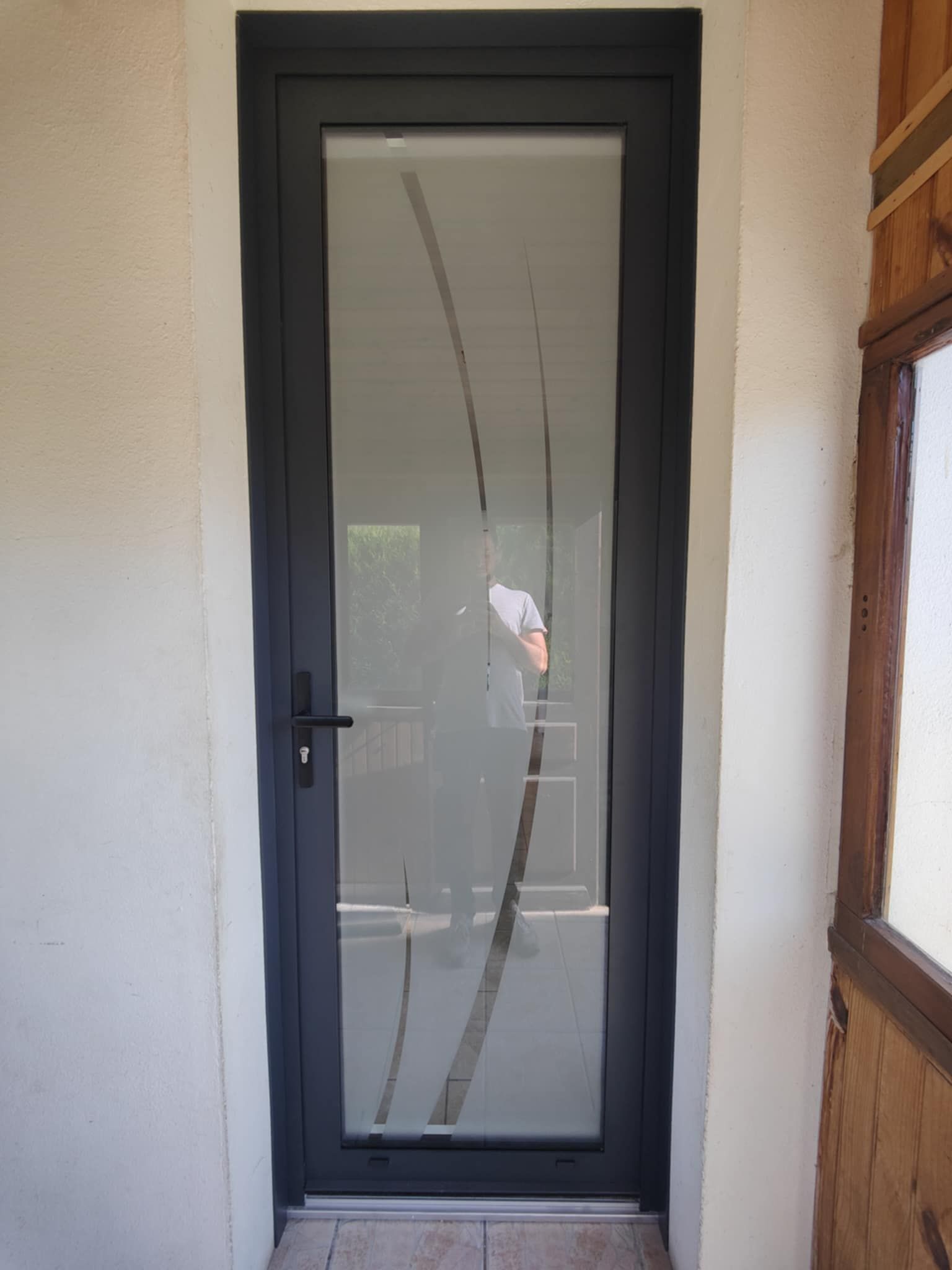 Porte d’entrée vitrée à cadre noir, avec des bandes verticales dépolies et une poignée à gauche
