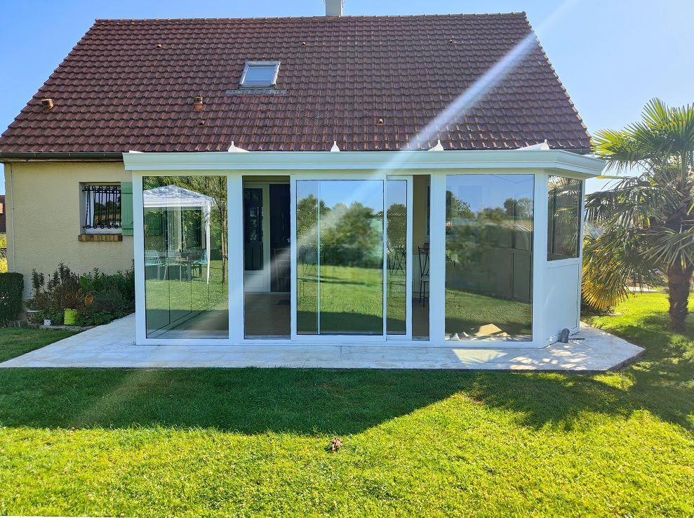 Maison moderne avec une extension vitrée blanche faisant office de véranda et une pelouse verte devant