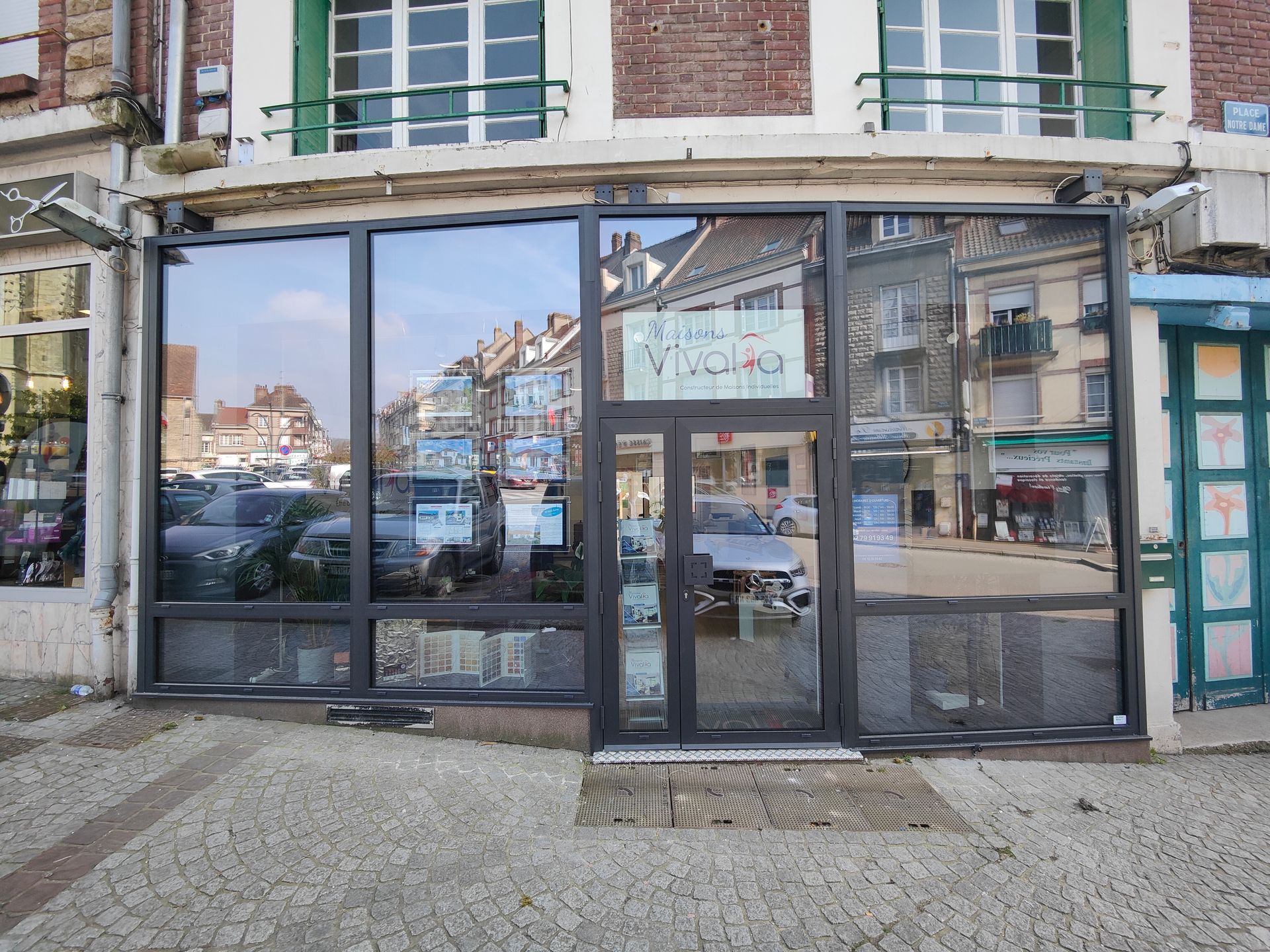 Entrée vitrée de magasin reflétant les bâtiments voisins et les voitures garées dans une scène de rue