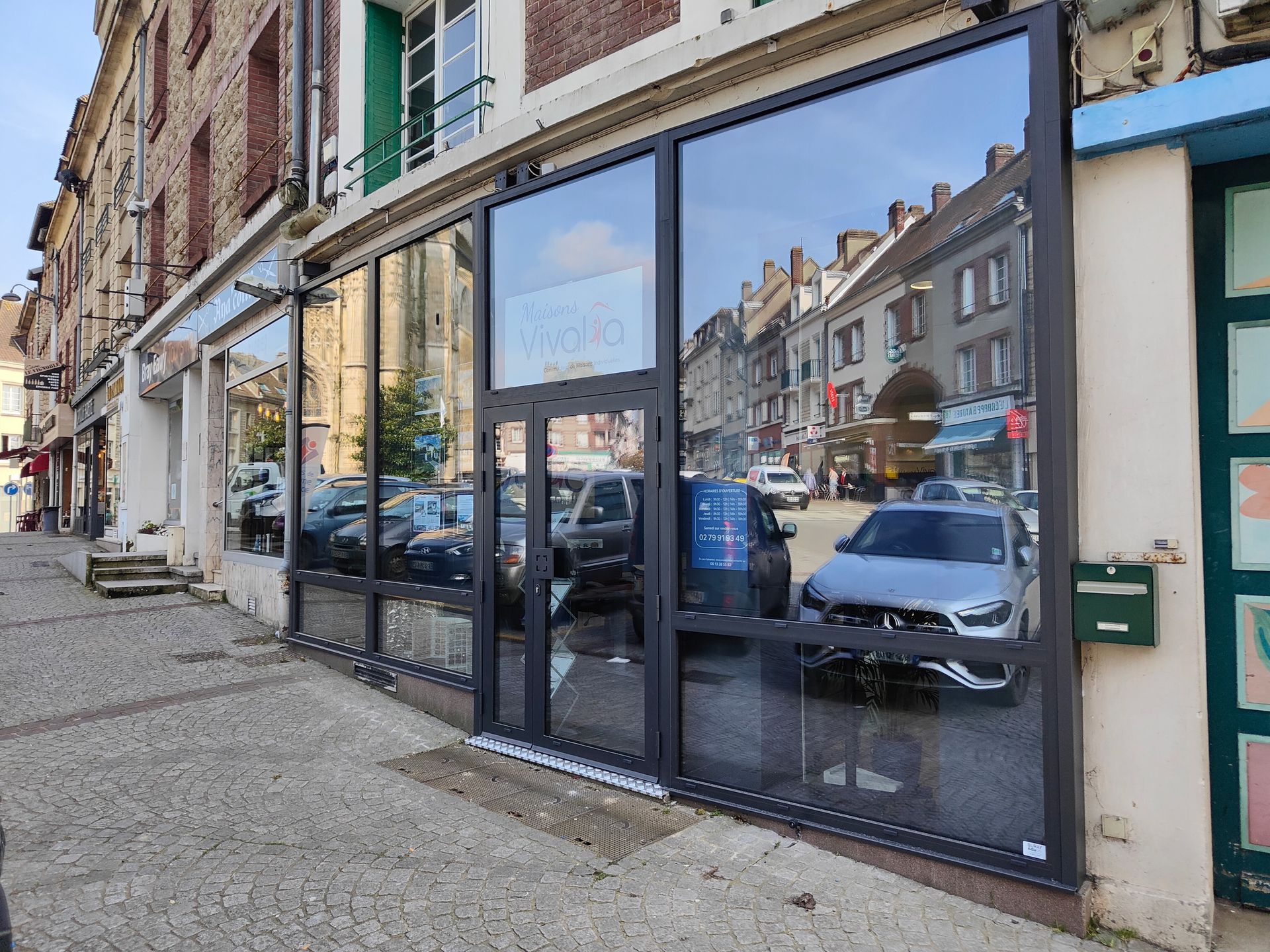 Vitrine en verre donnant sur une rue étroite en ville, reflétant des voitures garées et des maisons mitoyennes