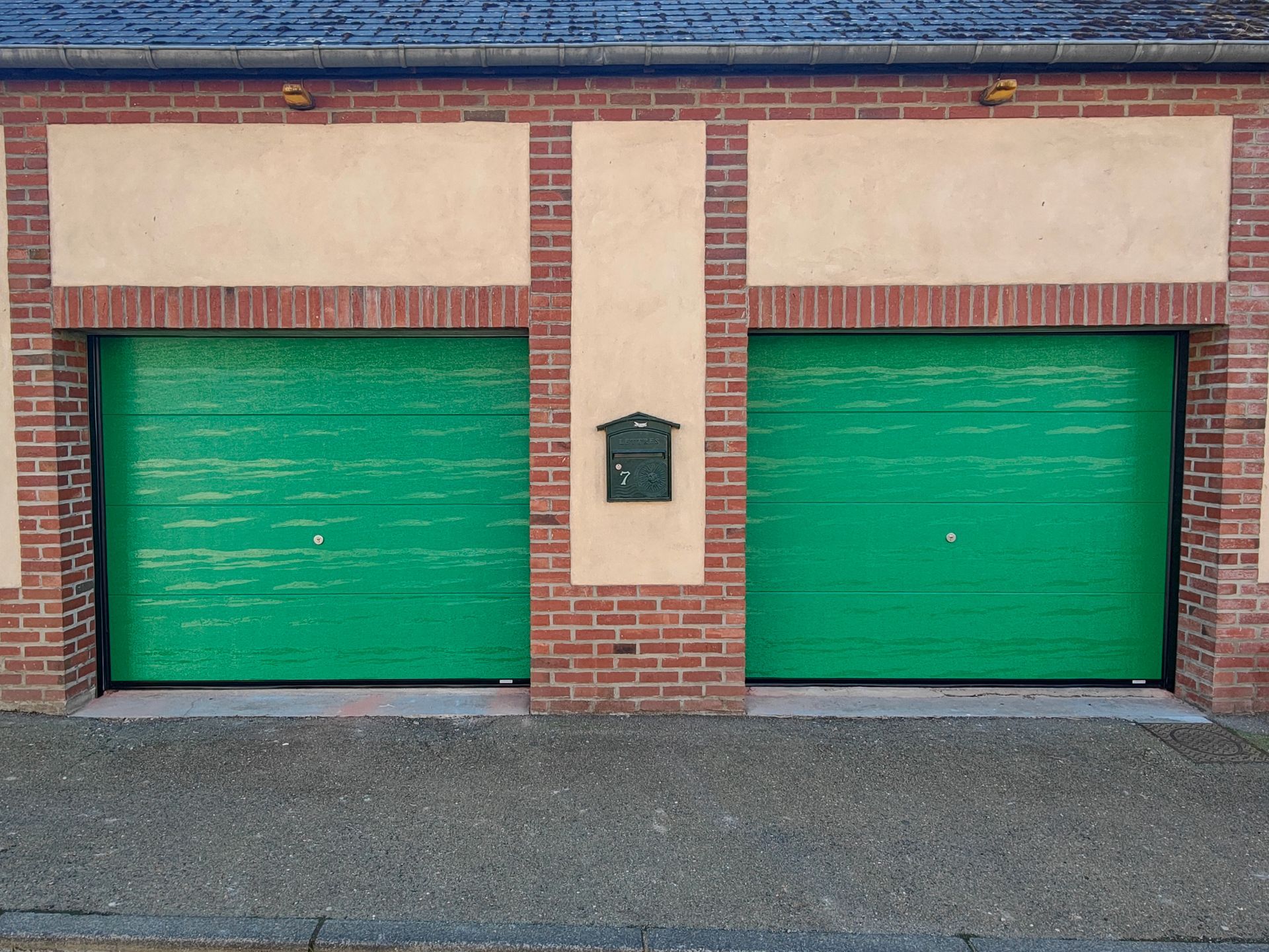 Deux portes de garage vertes dans un immeuble en briques avec une boîte aux lettres au centre