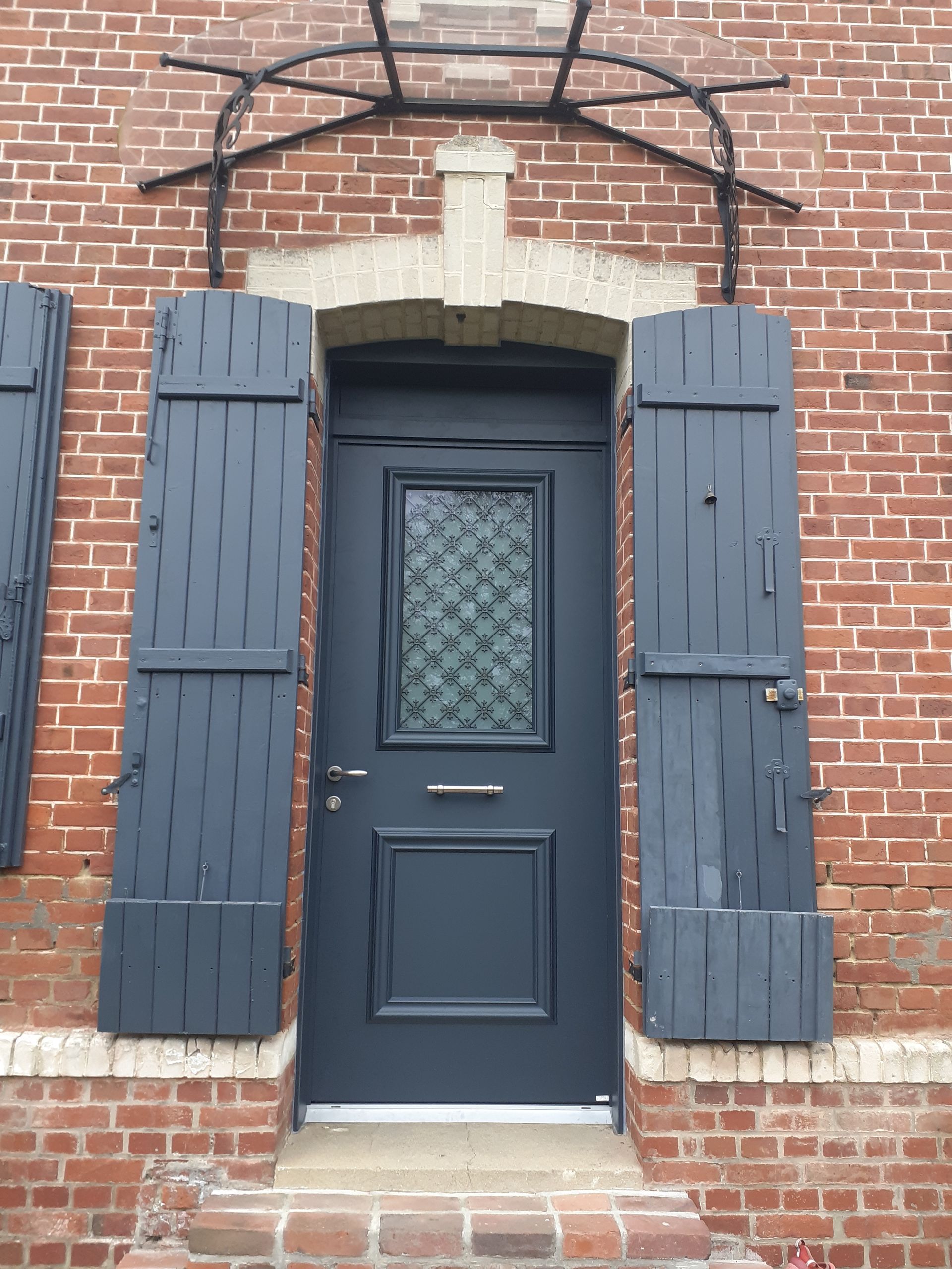 Porte d’entrée bleu foncé avec volets et encadrement en brique cintré sur une maison en briques