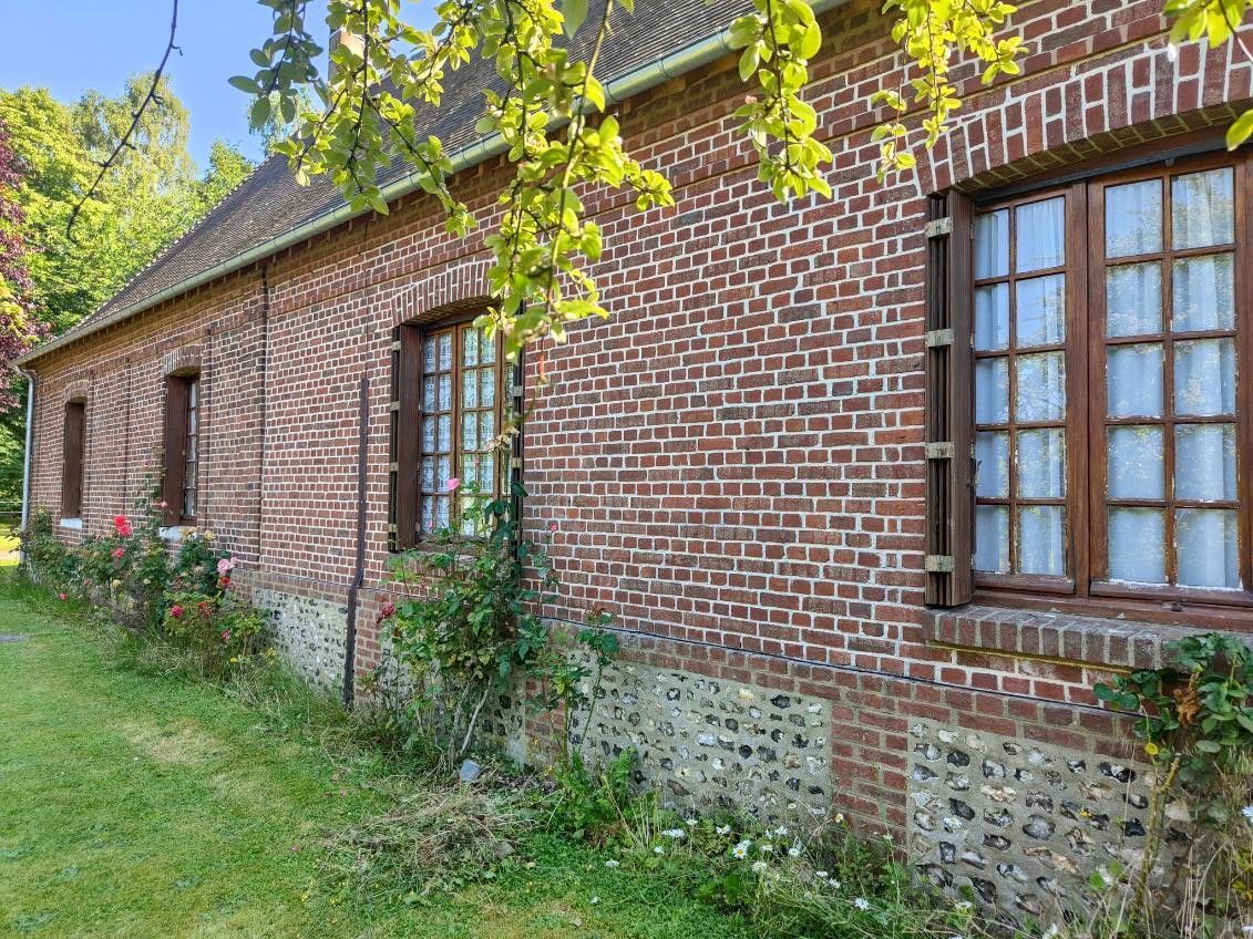 Ferme en briques couverte de lierre, avec un toit de tuiles rouges et des fenêtres, bordée d’un chemin herbeux et d’arbres