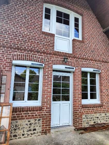 Façade d’un bâtiment en briques rouges, avec des fenêtres à encadrement blanc et une porte blanche sous une ligne de toiture arquée