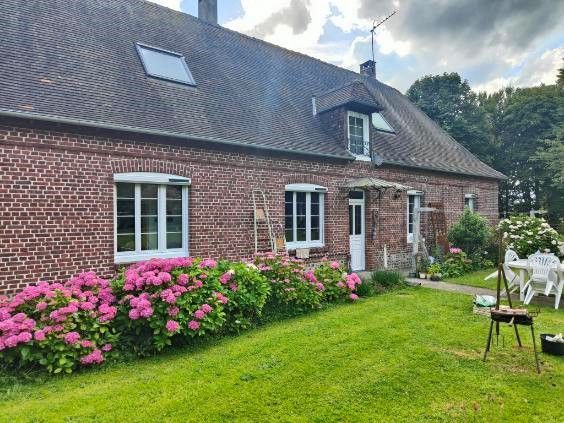 Cottage en briques avec des hortensias roses, une pelouse verte et des chaises de jardin blanches sous un ciel nuageux