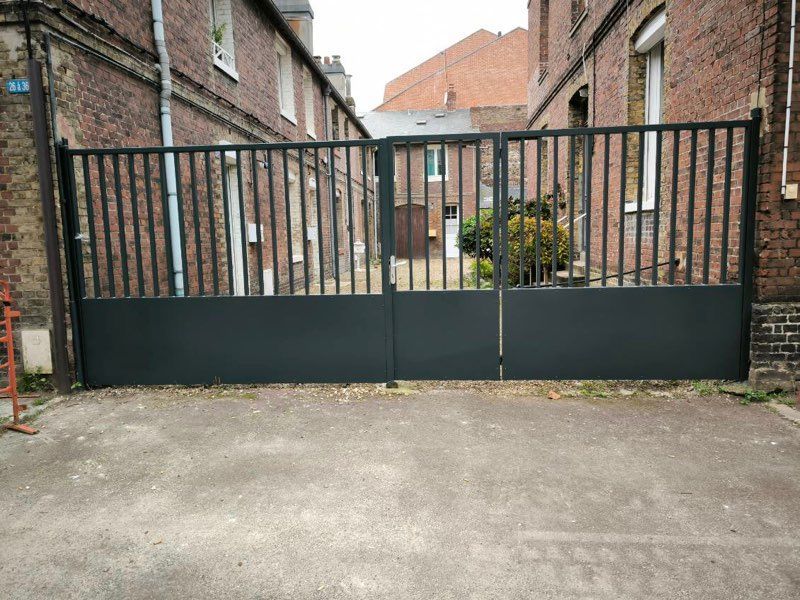 Portail noir en métal fermé entre des bâtiments en briques dans une ruelle