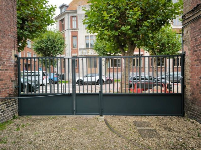 Portail fermé en métal noir devant un bâtiment en briques et des voitures en stationnement