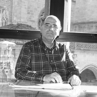 Un hombre con una camisa a cuadros está sentado en una mesa frente a una ventana.