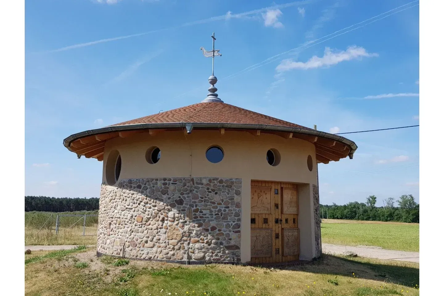 Ein kleines rundes Steingebäude mit einem Ziegel Dach und einer Wetterfahne darauf.
