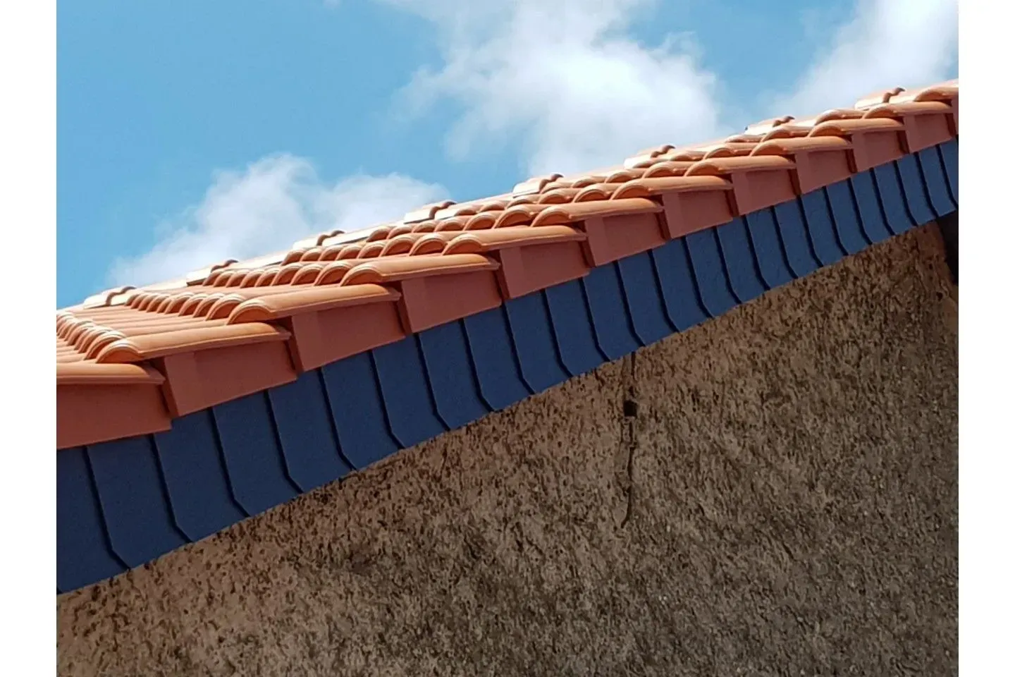 Ein Dach mit roten Ziegeln und einer Schieferverkleidung als Übergang zur Hauswand.