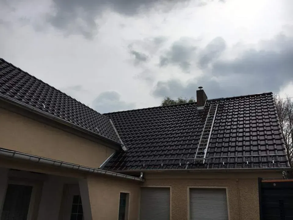 Ein Haus mit einem schwarzen Ziegeldach und neuen Schneefanggittern.