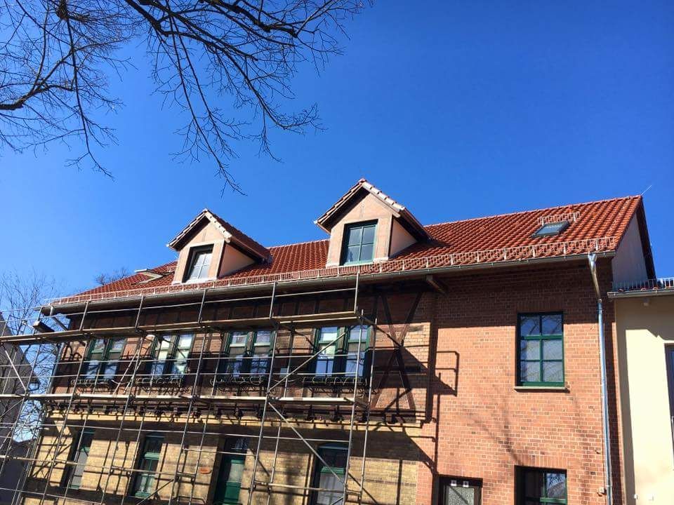 Ein Backsteingebäude mit einem roten Ziegeldach, das neu gedeckt wird.