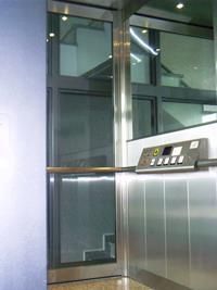 Ein Edelstahlaufzug mit einer Glastür und Treppen im Hintergrund.