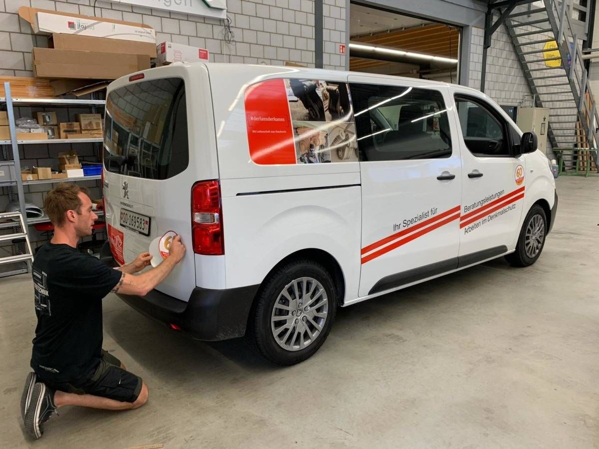 Ein Mann kniet in einer Garage und reinigt einen weissen Lieferwagen mit roten Streifen.