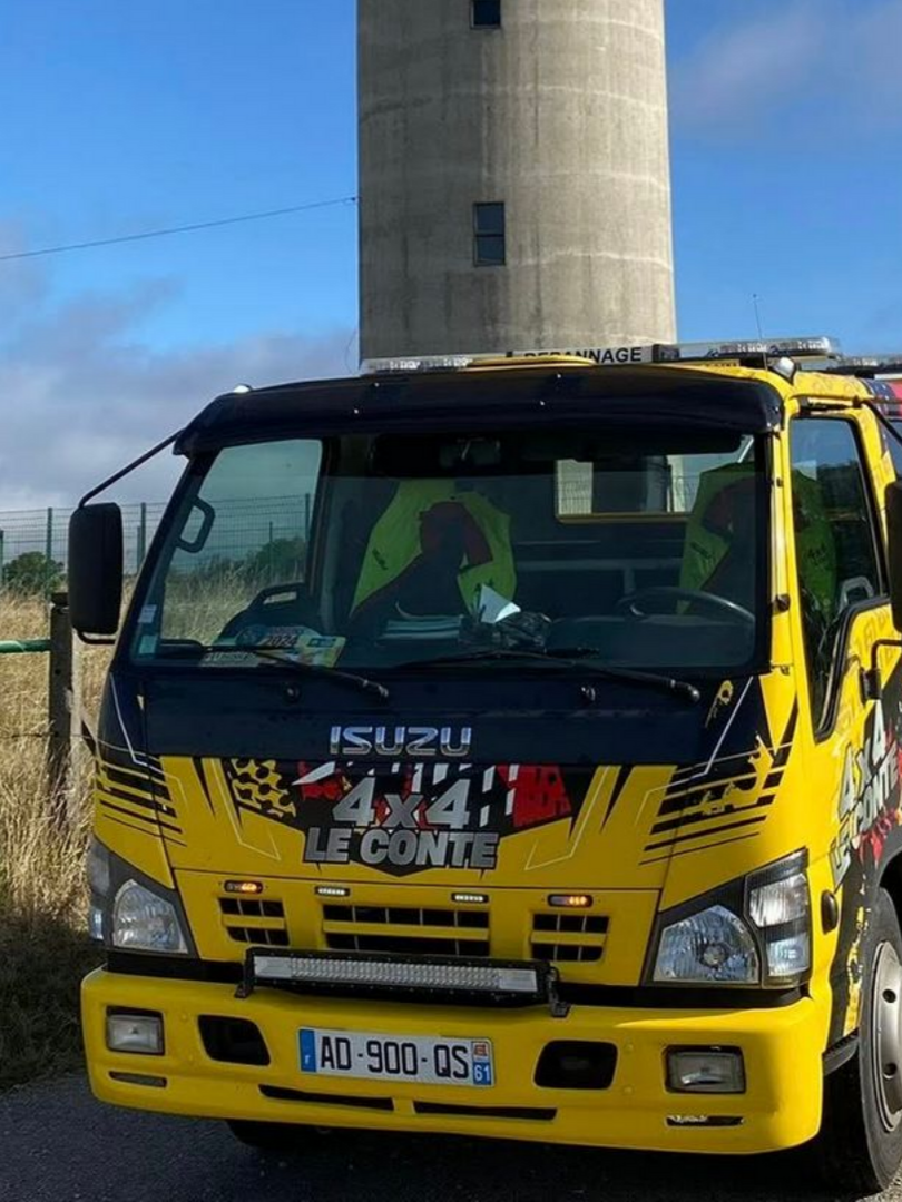 Dépanneuse Isuzu jaune devant une tour en béton par une journée ensoleillée.