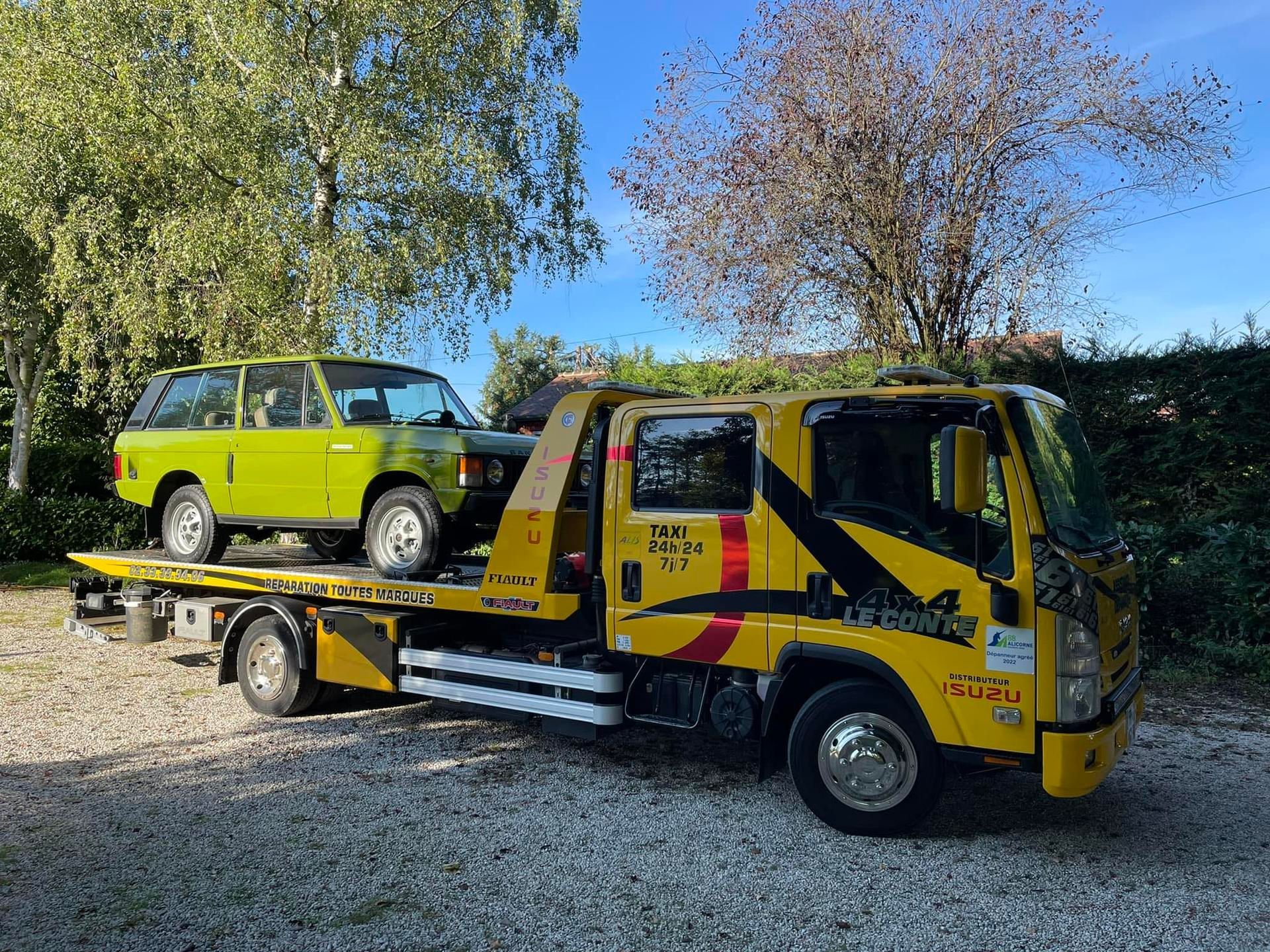 Dépanneuse jaune transportant un Range Rover vert clair par une journée ensoleillée.