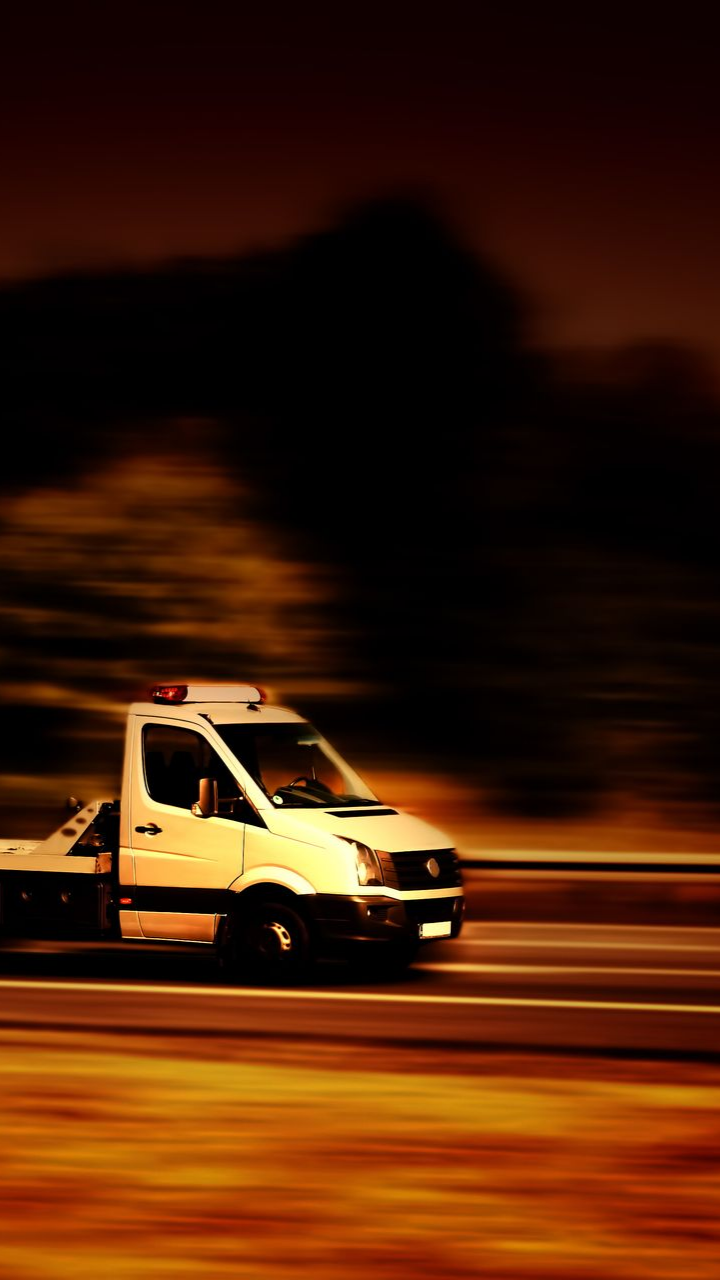 Dépanneuse roulant sur une autoroute au crépuscule. Tons jaunes et orange.