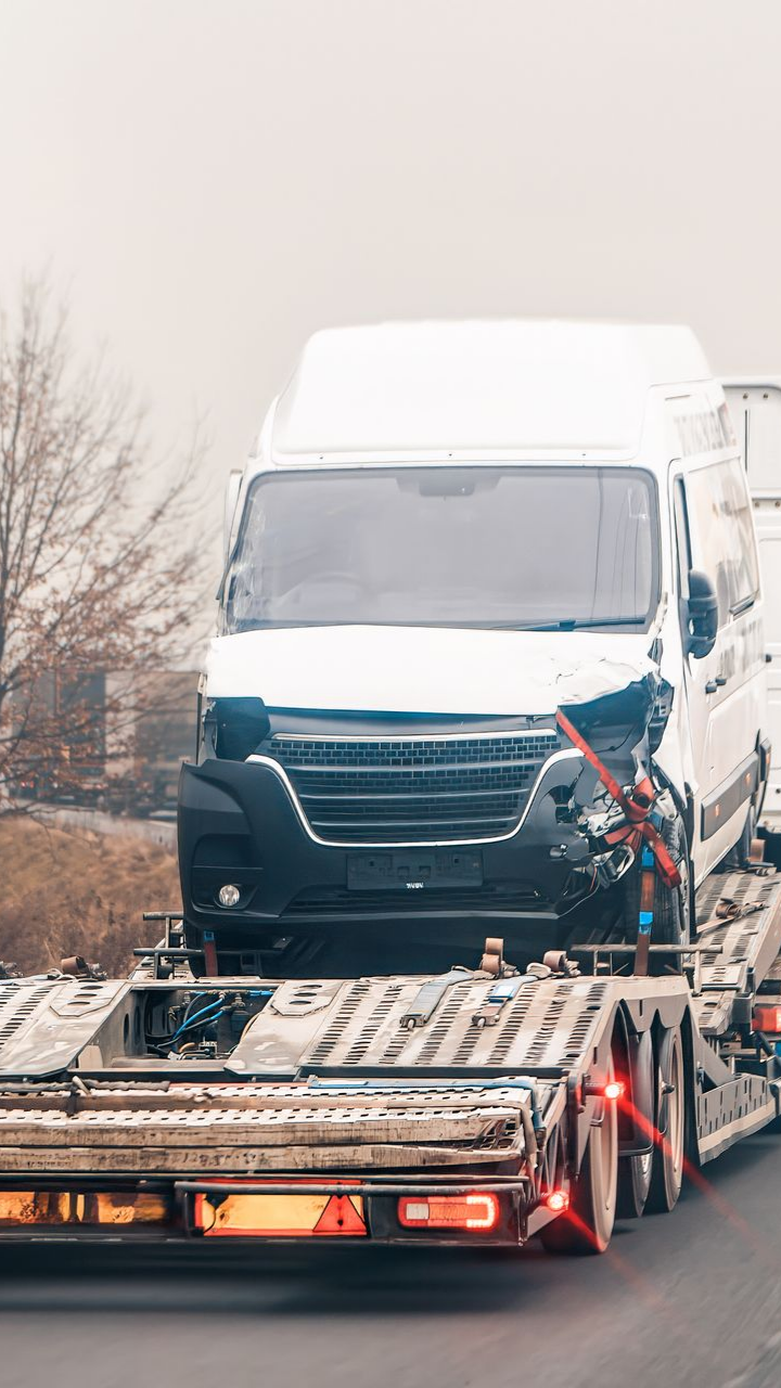 Fourgonnette blanche endommagée sur une dépanneuse à plateau, sur une route avec un arrière-plan flou.
