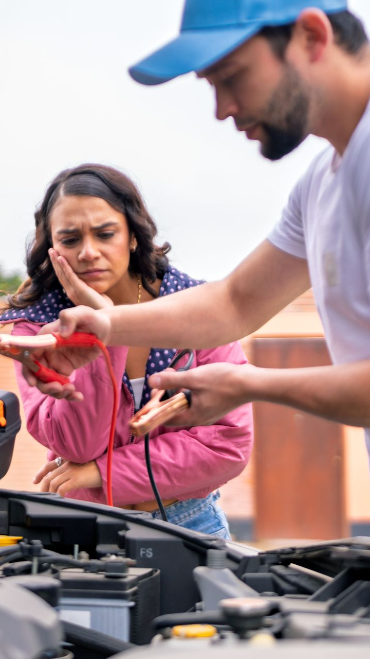Un homme aide une femme à faire démarrer sa voiture, tous deux l'air inquiet ; dehors.