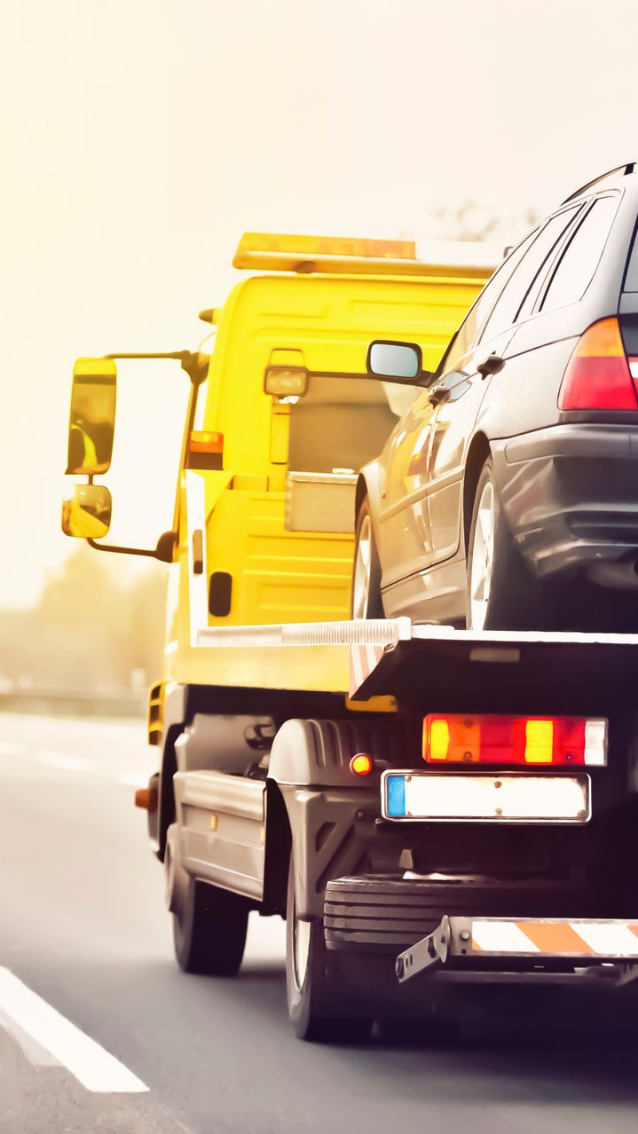 Dépanneuse jaune transportant une voiture noire sur une autoroute.