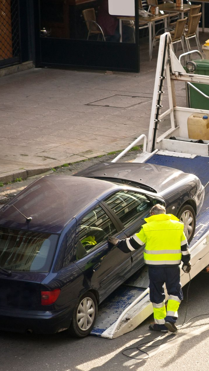 Une voiture remorquée par une dépanneuse, guidée par un ouvrier en veste fluo.