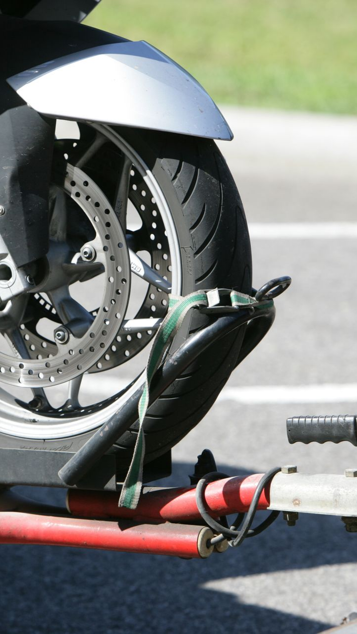 Roue de moto fixée à une remorque rouge avec une sangle verte sur l'asphalte.