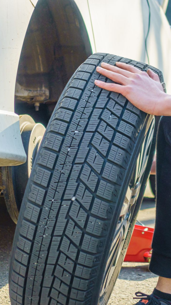 Une personne tenant un pneu d’hiver à côté d’une voiture.