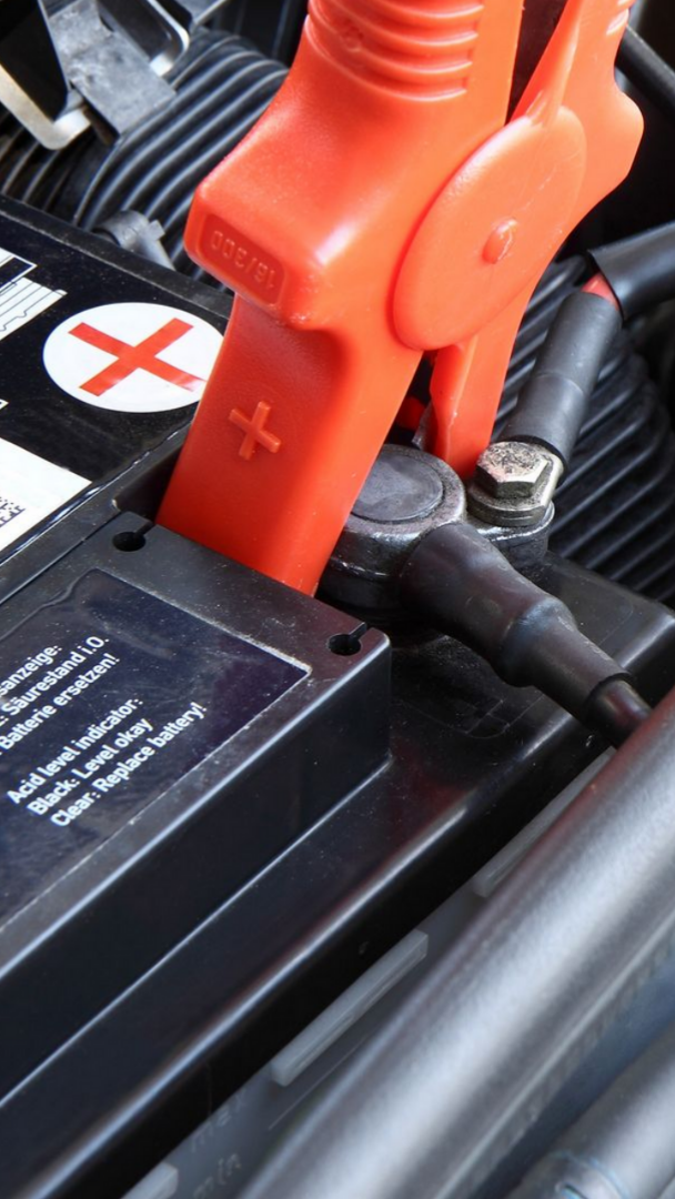 Pince de câble de démarrage rouge connectée à la borne positive d'une batterie de voiture.