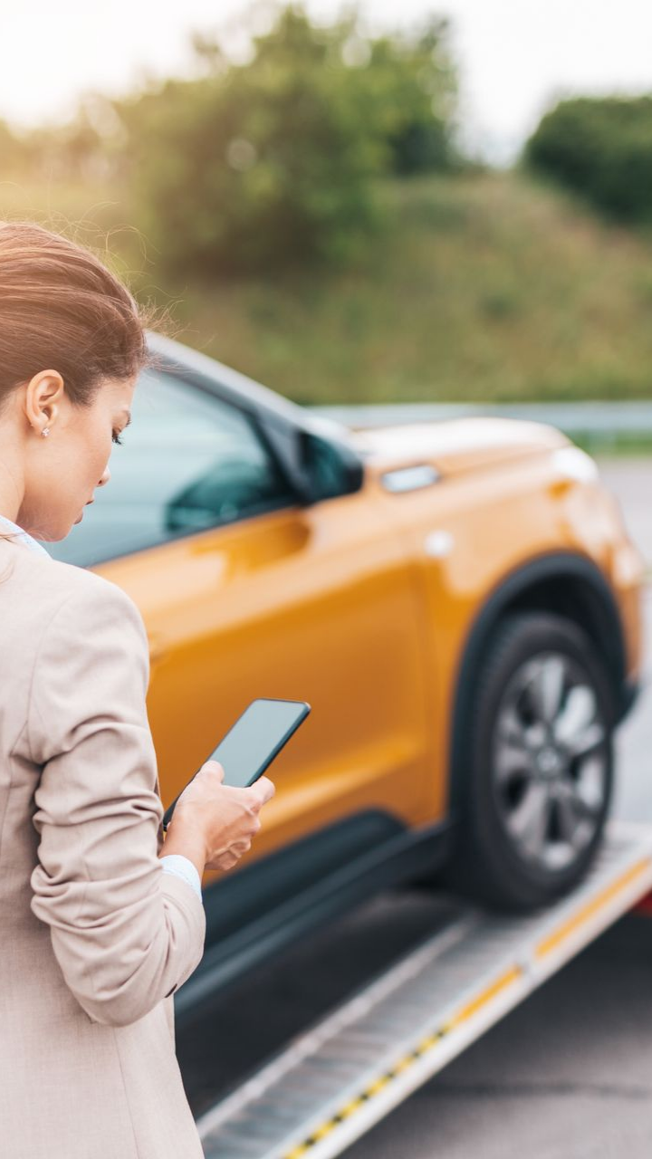 Femme au téléphone, voiture remorquée sur une rampe de camion, à l'extérieur, ensoleillé.