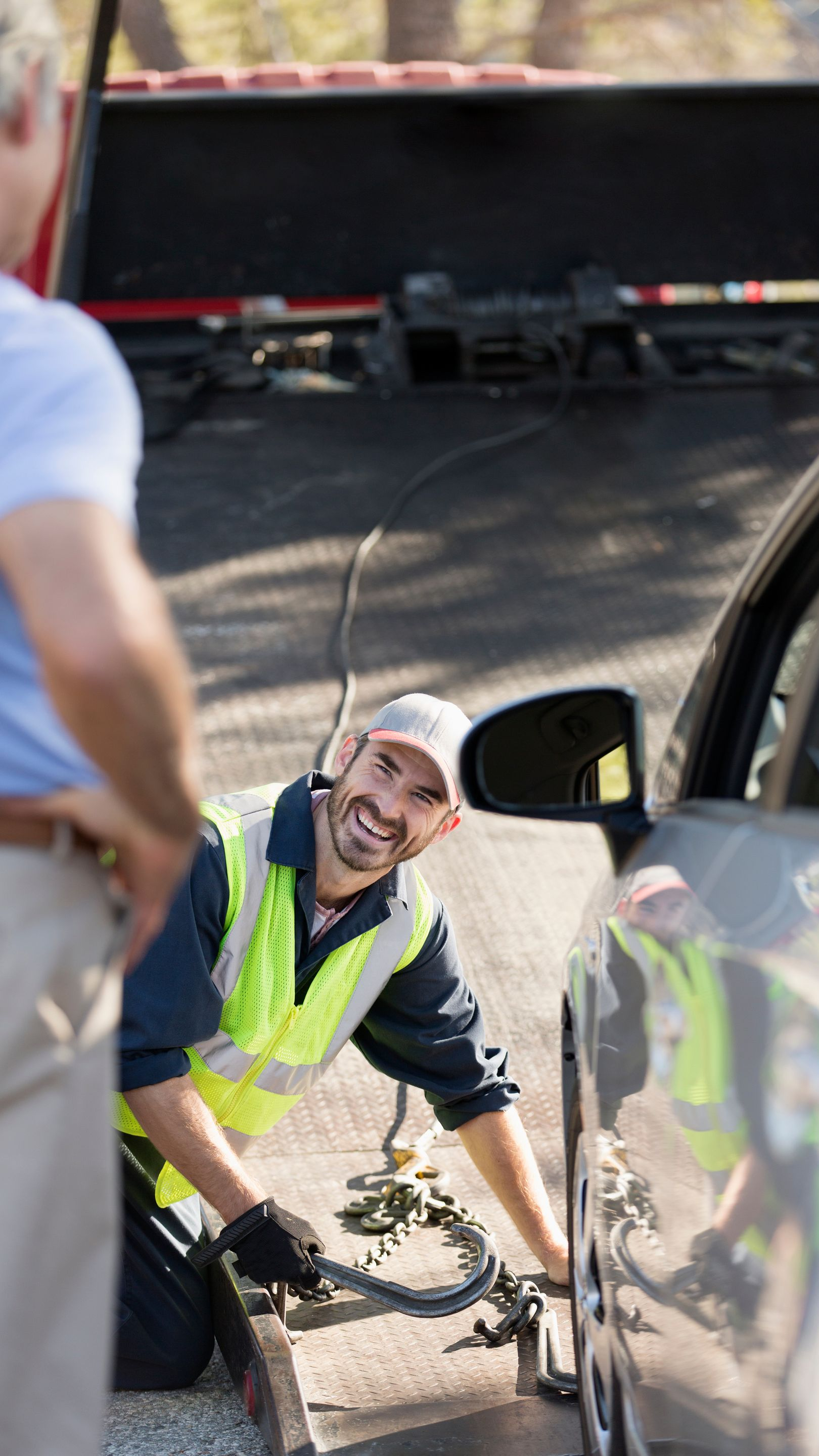 Un opérateur de dépanneuse attache un véhicule à une plateforme et sourit à un homme debout à proximité.