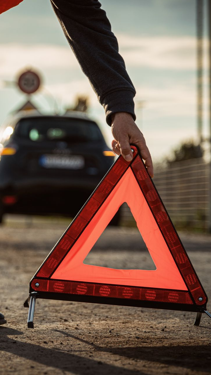 Une personne place un panneau d'avertissement triangulaire réfléchissant rouge sur le bord de la route à côté d'une voiture.