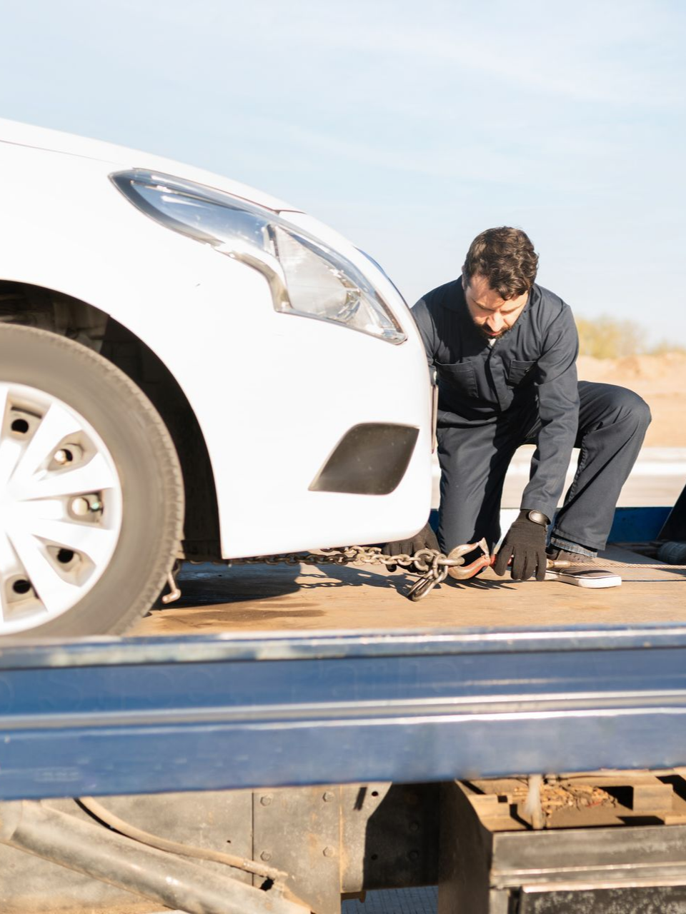 Un homme en salopette attache une voiture à une dépanneuse.