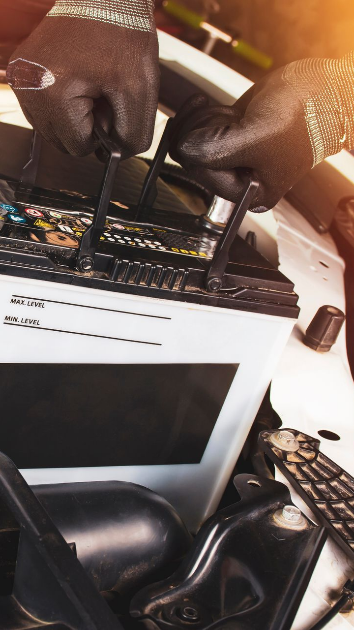 Des mains gantées de noir connectent les bornes de la batterie d'une voiture dans un compartiment moteur.