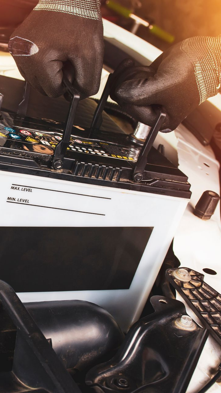 Un mécanicien en gants noirs travaille sur une batterie de voiture sous le capot.