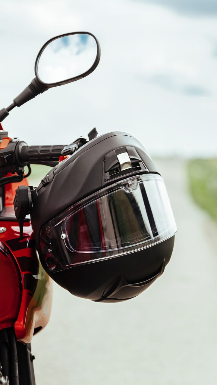 Casque noir accroché sur un guidon de moto rouge avec une route en arrière-plan.