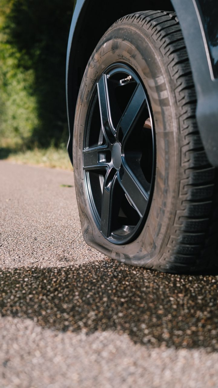 Pneu crevé sur une roue noire sur une route, avec des flaques d'eau.