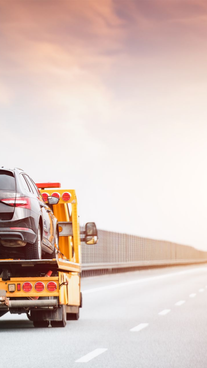 Une dépanneuse transportant une voiture noire sur une autoroute au coucher du soleil.