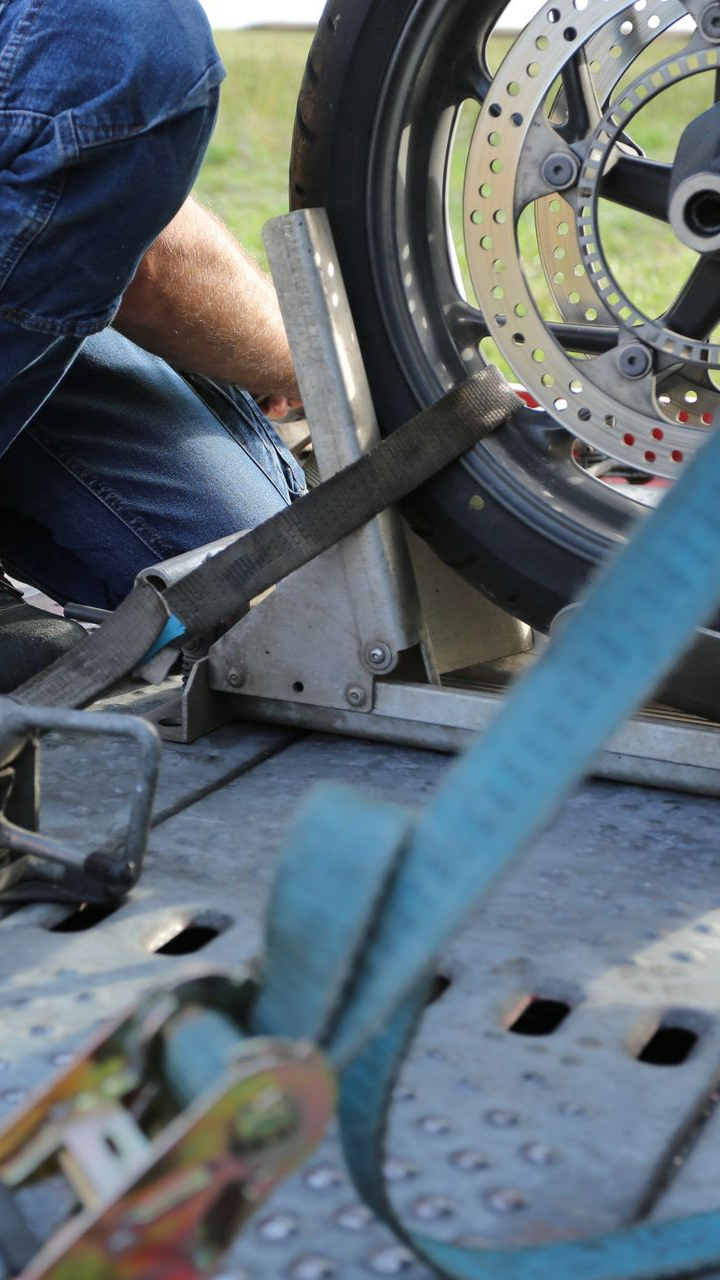 Moto attachée à une remorque avec des sangles. Une personne en jean travaille dessus.