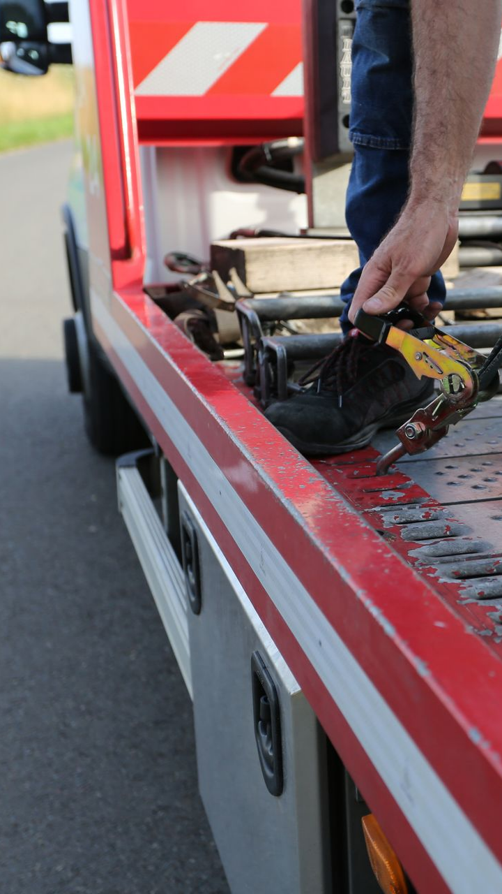 Personne sur une dépanneuse rouge cherchant un treuil, en bord de route.
