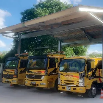 Trois dépanneuses jaunes garées sous un espace couvert.