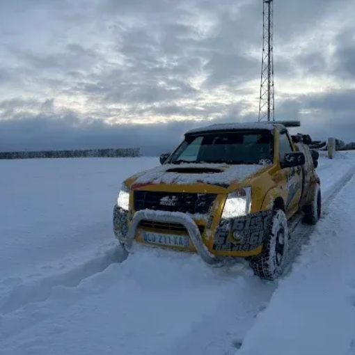Un camion jaune circule dans un champ enneigé sous un ciel nuageux.