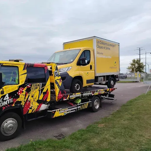 Dépanneuse transportant un camion de livraison jaune sur une route pavée, ciel couvert.
