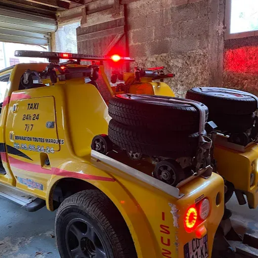 Dépanneuse jaune avec feux clignotants, pneus de secours et panneau TAXI, garée dans un garage.