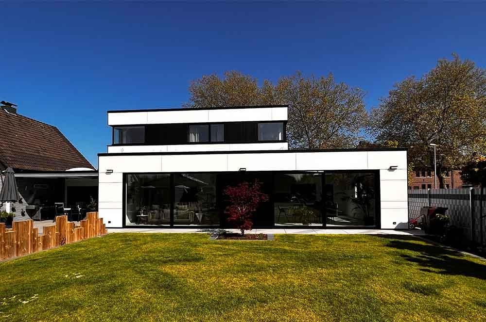 Ein großes weißes Haus mit vielen Fenstern steht auf einem üppigen grünen Rasen.