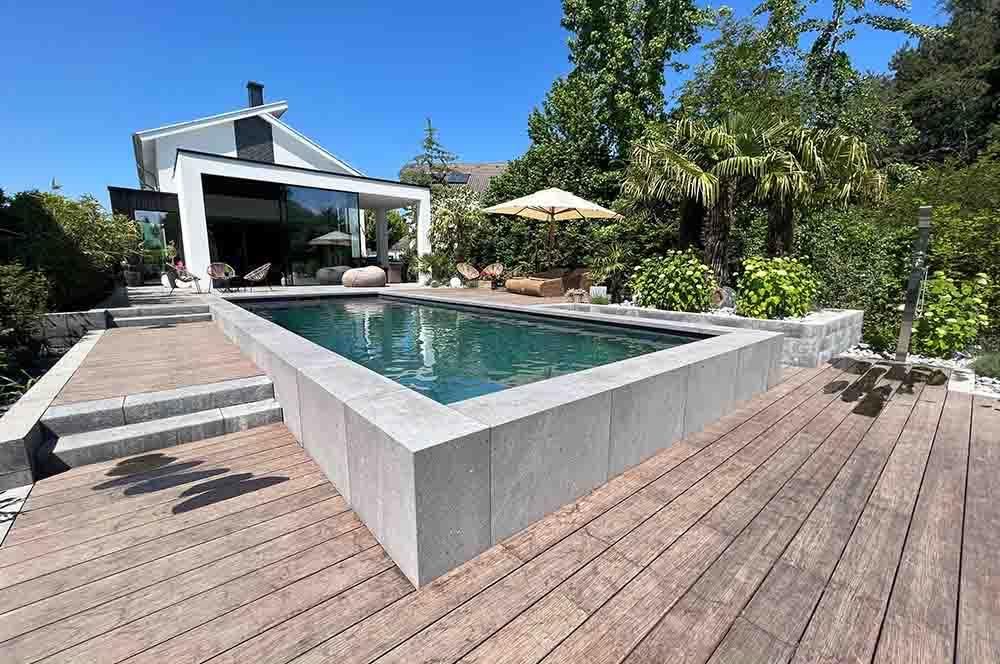 Vor einem Haus ist ein großer Swimmingpool von einer Holzterrasse umgeben.